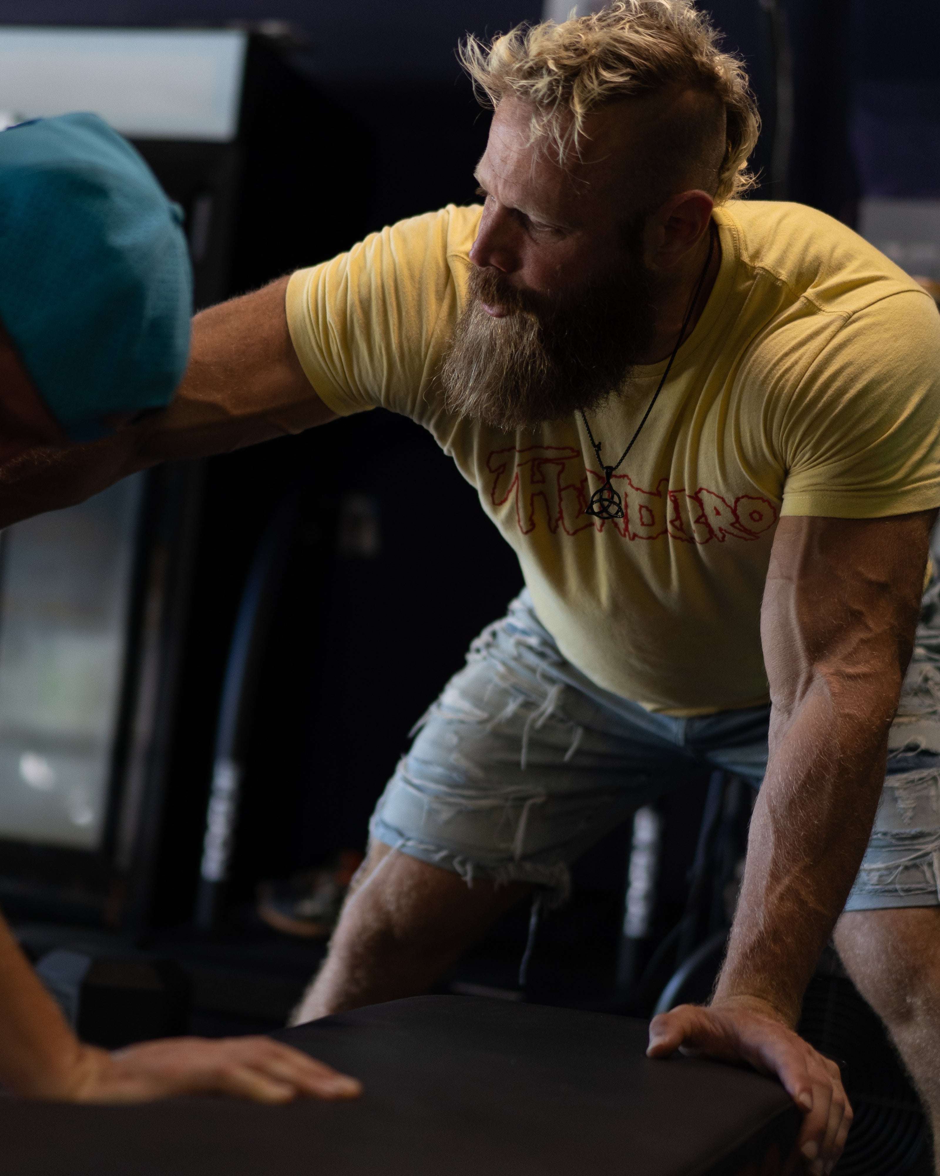 Two men in a gym setting, one assisting the other with exercise equipment.